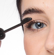 Žena si nanáší řasenku kartáčkem, čímž dodává řasám objem a zdokonaluje oční make-up.